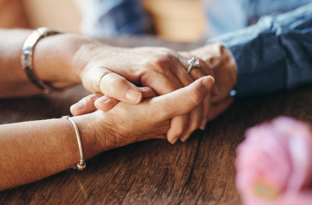 A couple holding hands on a brown wood tabletop.